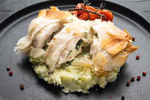 Stuffed chicken meat with filo, with baked cherry tomatoes, mashed potatoes, on black stone background