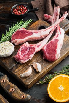 Frenched raw fatty lamb chops, with ingredients carrot orange, herbs, on old dark wooden table background