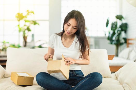 A young woman is sitting on the sofa and is happily unpacking her package