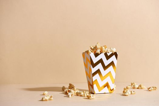 Salty fresh crusty homemade popcorn in golden paper cup in the fashion beige background in a New Year"s interior. selective focus