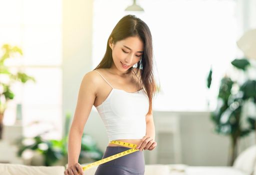 A young woman at home confidently measured her waist circumference, satisfied with her posture, and very happy to lose weight