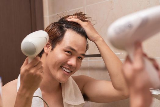 Young asian man blow drying hair in bathroom
