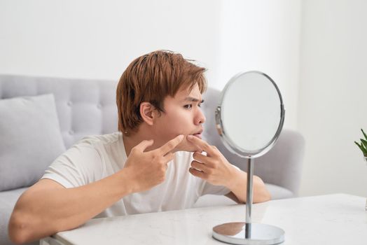 Asian man looking at mirror and popping a pimple