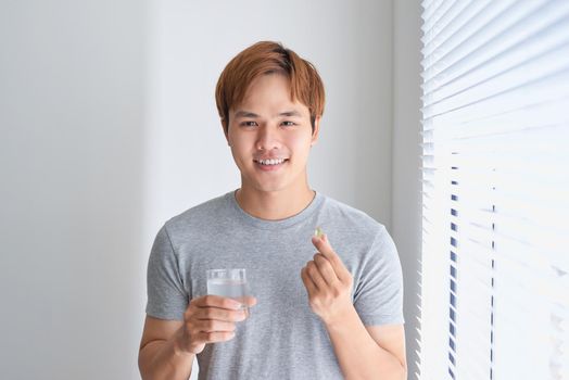 Happy asian man holding omega 3 vitamin pill at home 