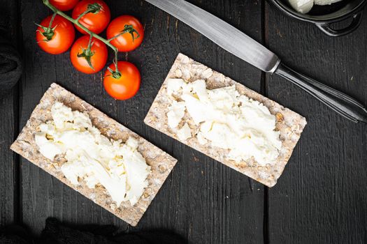 Wholegrain Rye Crispbread with cream cheese, on black wooden table background, top view flat lay