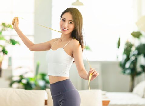 A young woman at home, holding a measuring ruler while dancing, is very satisfied with her posture, very happy to lose weight