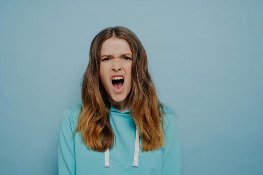 Pretty teenage girl expressing angry disbelief posing isolated over blue background