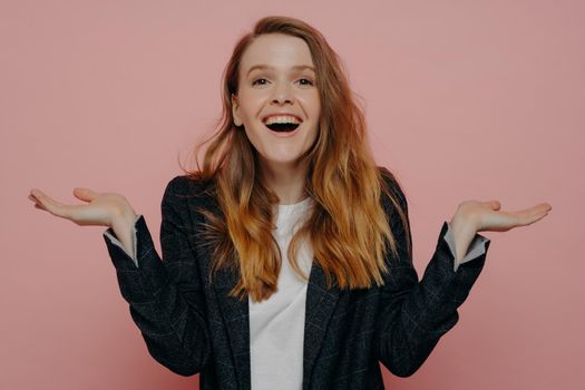 Excited young woman posing with open palm gesture over pink background
