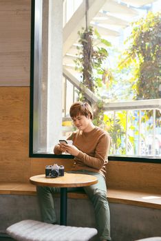 Young Asian man using smart phone during having breakfast, coffee time and summer holiday vacation concepts