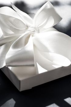 Luxury holiday white gift box with silk ribbon and bow on black background, luxe wedding or birthday present