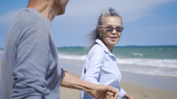 senior man and woman couple holding hands walking to the beach sunny with bright blue sky