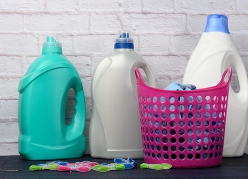 pink laundry basket and plastic bottles with liquid detergent on white brick wall background