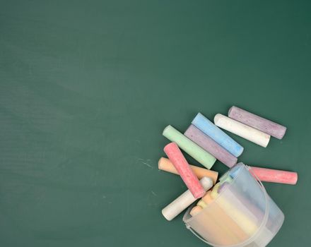 multicolored crayons on the background of green chalk school blackboard