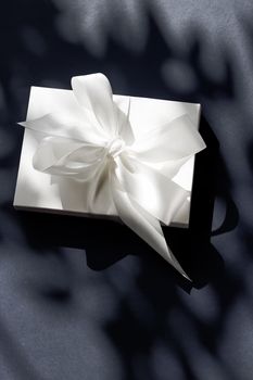 Luxury holiday white gift box with silk ribbon and bow on black background, luxe wedding or birthday present