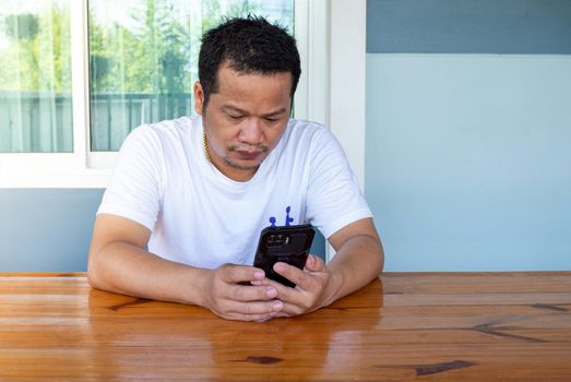 Asian man wearing white shirt using the phone on a wooden table