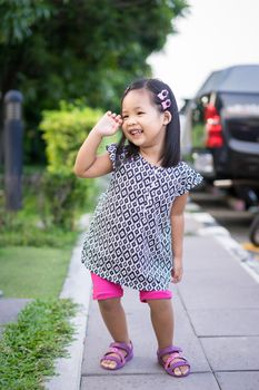 Portrait of happy asian little girl in dress standing on footpath in the park