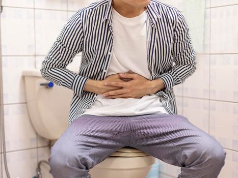 Young man holding his abdomen feels sick and constipation in the toilet