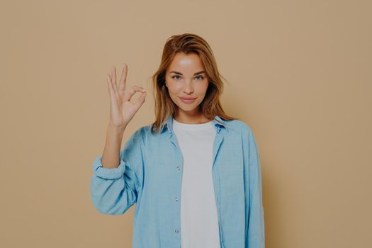 Young lady expressing approval with okay gesture on beige background