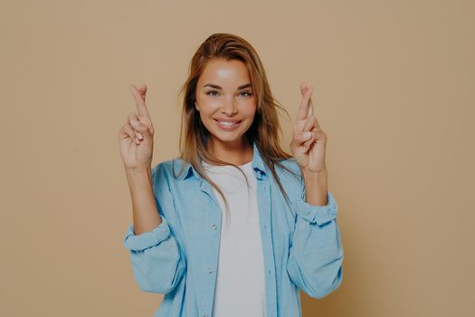 Positive lady with fingers crossed on beige background