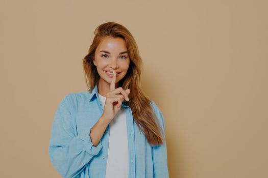 Excited woman showing silence gesture on beige background