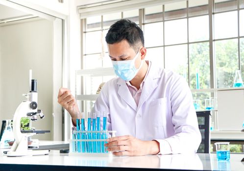 Asian scientists or chemists experiment with droplets of blue liquid chemicals in a laboratory.