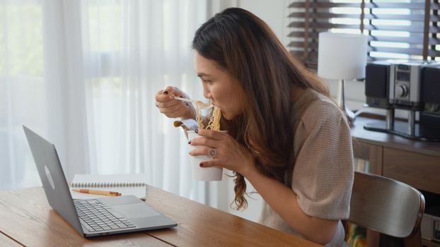 business woman eating instant noodles while working on laptop computer