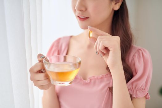 Young woman with glass of water taking vitamin pill at home