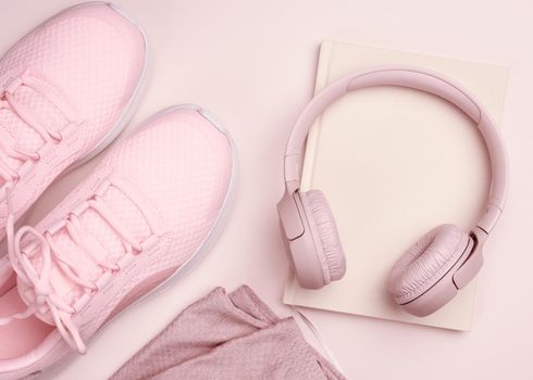 pink wireless headphones, a pair of sneakers and a notepad on a beige background, top view