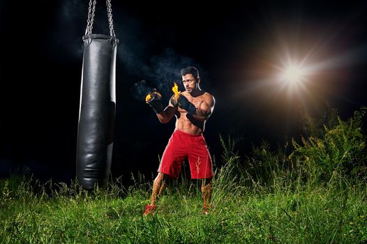 Professional boxer punching sandbag outdoors with his boxing glo