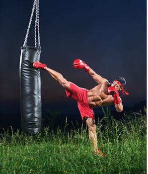 Young handsome male boxer practicing on a punching bag outdoors