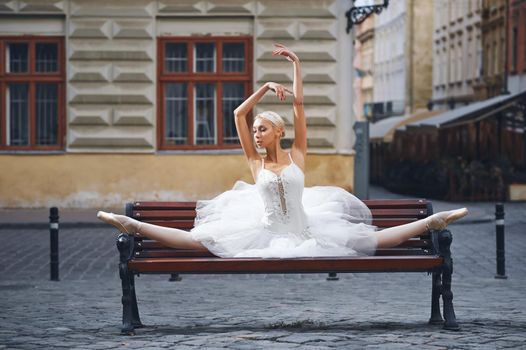 Attractive ballerina sitting on the bench in the city