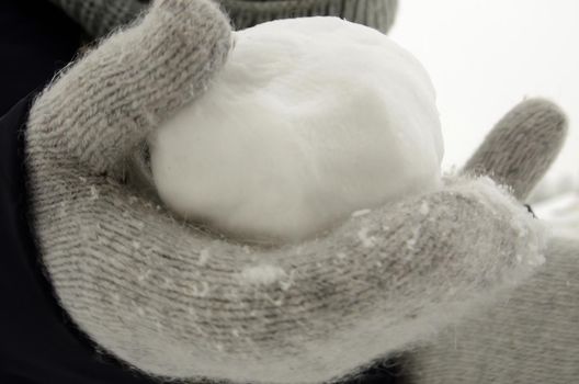 A snowball made from freshly plowed snow, in a hand in a gray woolen glove.