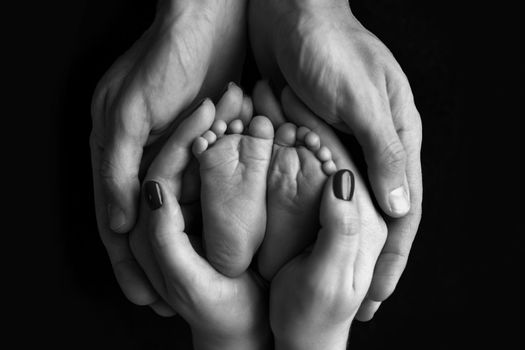 Children's feet in hold hands of mother and father. Mother, father and newborn.