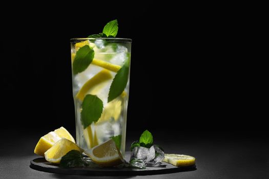 Fresh homemade cocktail with lemon, mint and ice on a dark background