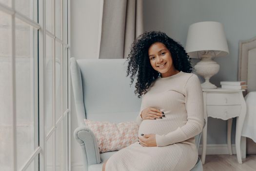 Positive pregnant woman touching gently her belly and smiling