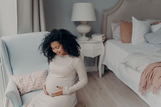 Lovely african american enjoying happy pregnancy while sitting in bedroom