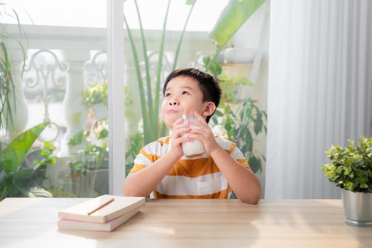 A asian boy drinking milk while sitting at desk after doing homework. E-learning and education concept.