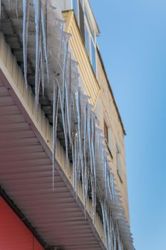 Long straight icicles hang from the roof dangerously to the bottom close-up. 