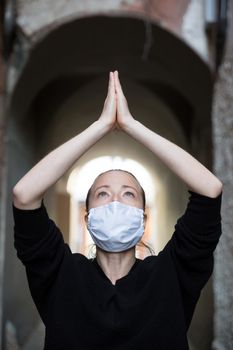 Coronavirus outbreak. Young caucasian woman wearing medical protection face mask praying over coronavirus global pandemic, for salvation of humanity, health, anxiety and depression reduction