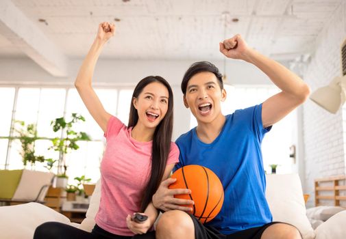 Young couple watching tv and raising hands to celebrating the victory