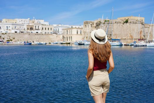 Beautiful young woman with hat looking at historic village of Gallipoli in Salento, Italy