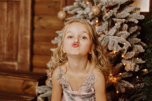 Little girl in a pink dress grimaces on the background of the Christmas tree