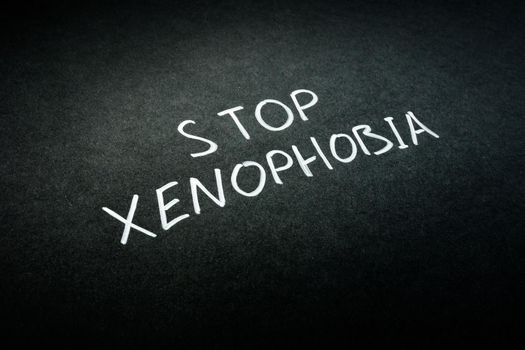 Stop xenophobia handwritten sign on black paper.
