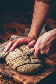 Baker slices loaf of homemade rye bread