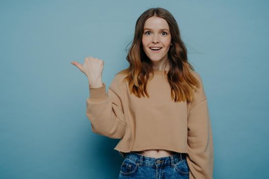 Excited young girl pointing finger somewhere posing over blue background