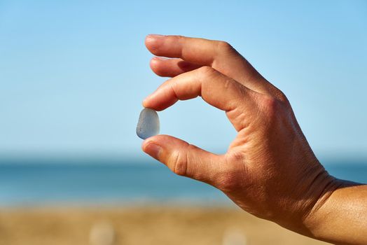 A person holds a single piece of blue sea glass between their finger and thumb